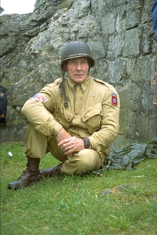 Original photo: A soldier in a tan uniform and helmet sitting beside a stone wall.