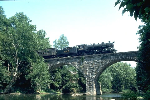 Original photo: A black steam train crossing a stone arch bridge above a river and green trees.